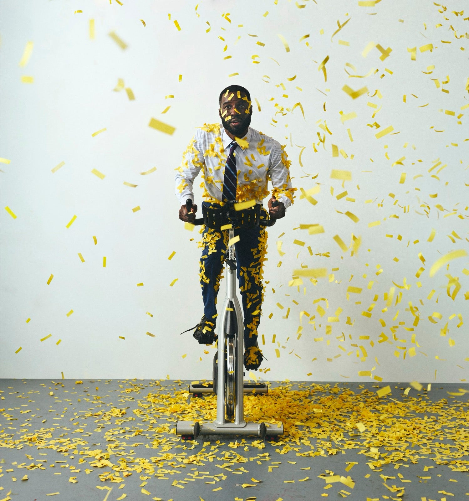 Marcus on a stationary bike in business clothes, hit by a blast of confetti